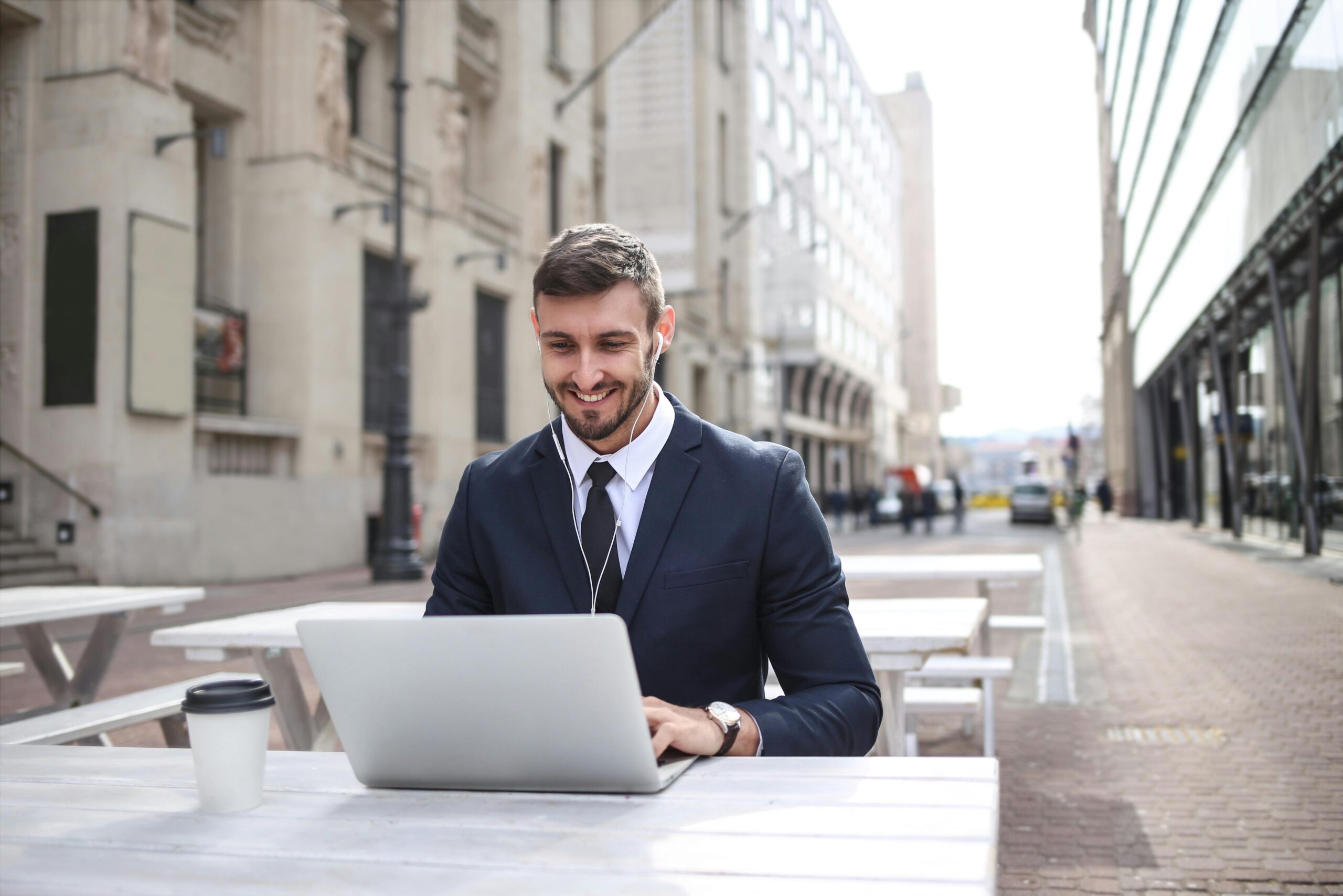 Professional man enjoying remote work on a laptop outdoors in a city setting.
